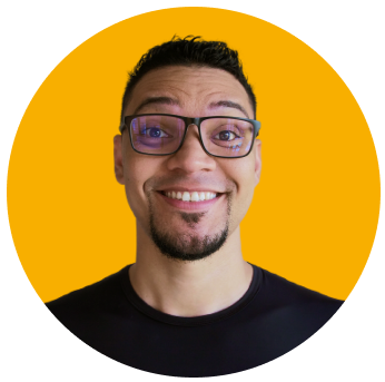 Foto de Mayk Brito sorrindo, usando oculos, camisa preta, barba e fundo amarelo